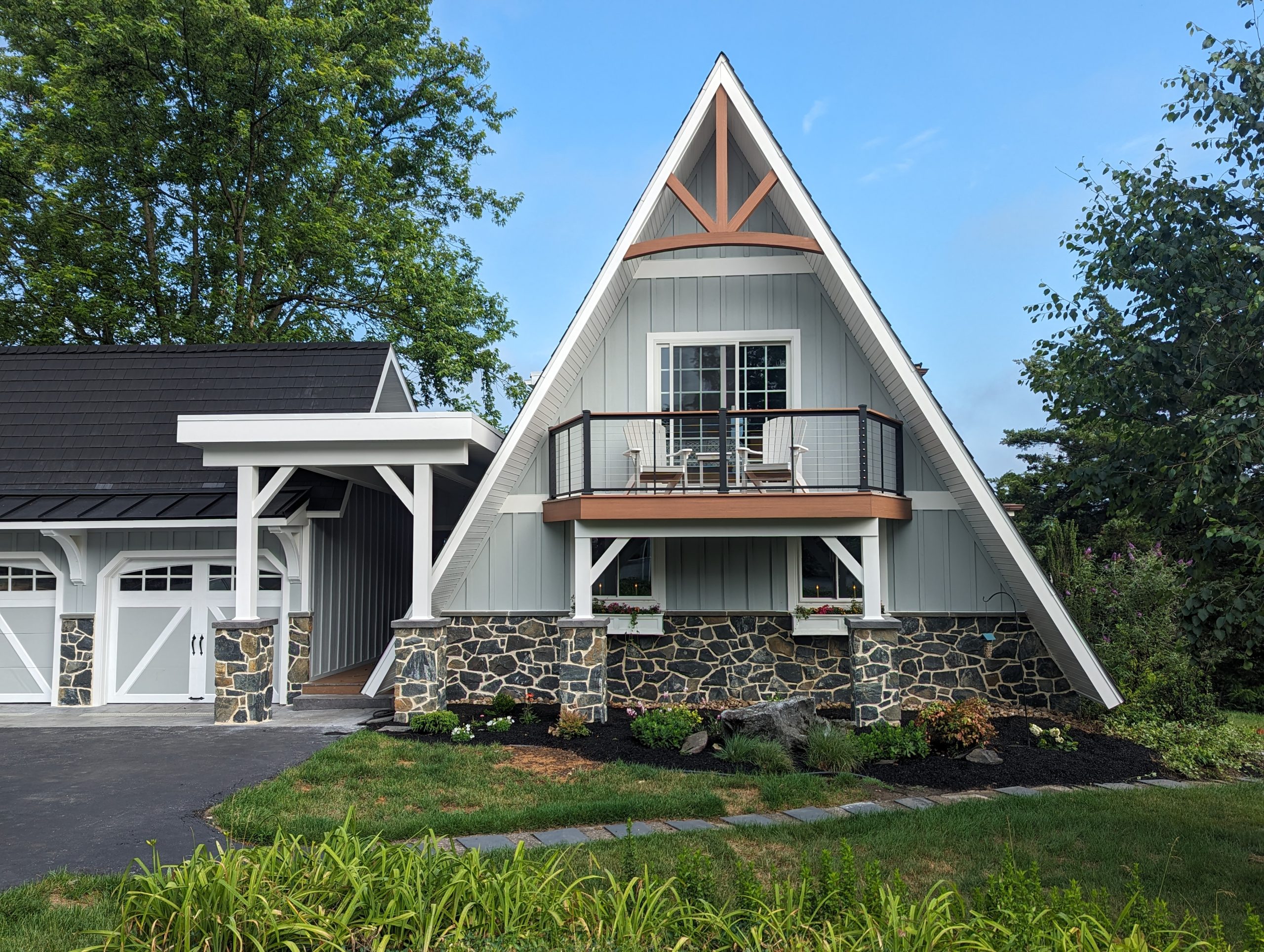Front exterior of a unique triangle shaped home with new light gray siding, white trim, stone accents, brown balcony, and a matching 2-car garage