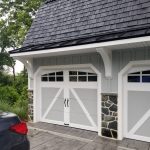 Close up of an exterior garage remodel with light gray siding, white trim, 2 garage doors, and black roofing.