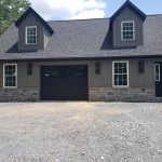 Remodeled attached garage with 1 black garage door, gray siding, dark roofing, and stone accents.