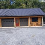 2 car barn garage with an overhang, black metal roofing, 2 black garage doors, rustic wood siding, rustic log posts, a single-entry red door with windows, and a large window.