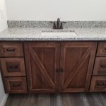 Bathroom sink vanity with brown wooden base and a speckled gray and white granite countertop.
