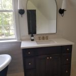 Close up of a new bath vanity with a dark base, white marble countertop, and an arched mirror.