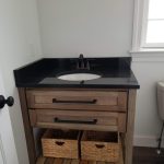 Bath vanity with skin, black granite countertop, and a brown stained wood base with an open shelf on the bottom.
