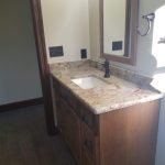 Large bathroom vanity with bronze faucet, white sink basin, tan patterned quartz countertop, a wood framed mirror, and a wood vanity base.