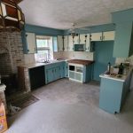 View of a kitchen before a remodel with blue walls, blue cabinets, white cabinet doors, and a brick fireplace.