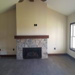 Stone electric fireplace with wood top in a room with light colored walls, a brown ceiling fan, and dark gray wood flooring.