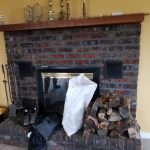 Close up of an old brick fireplace with a stack of wood and fireplace accessories.