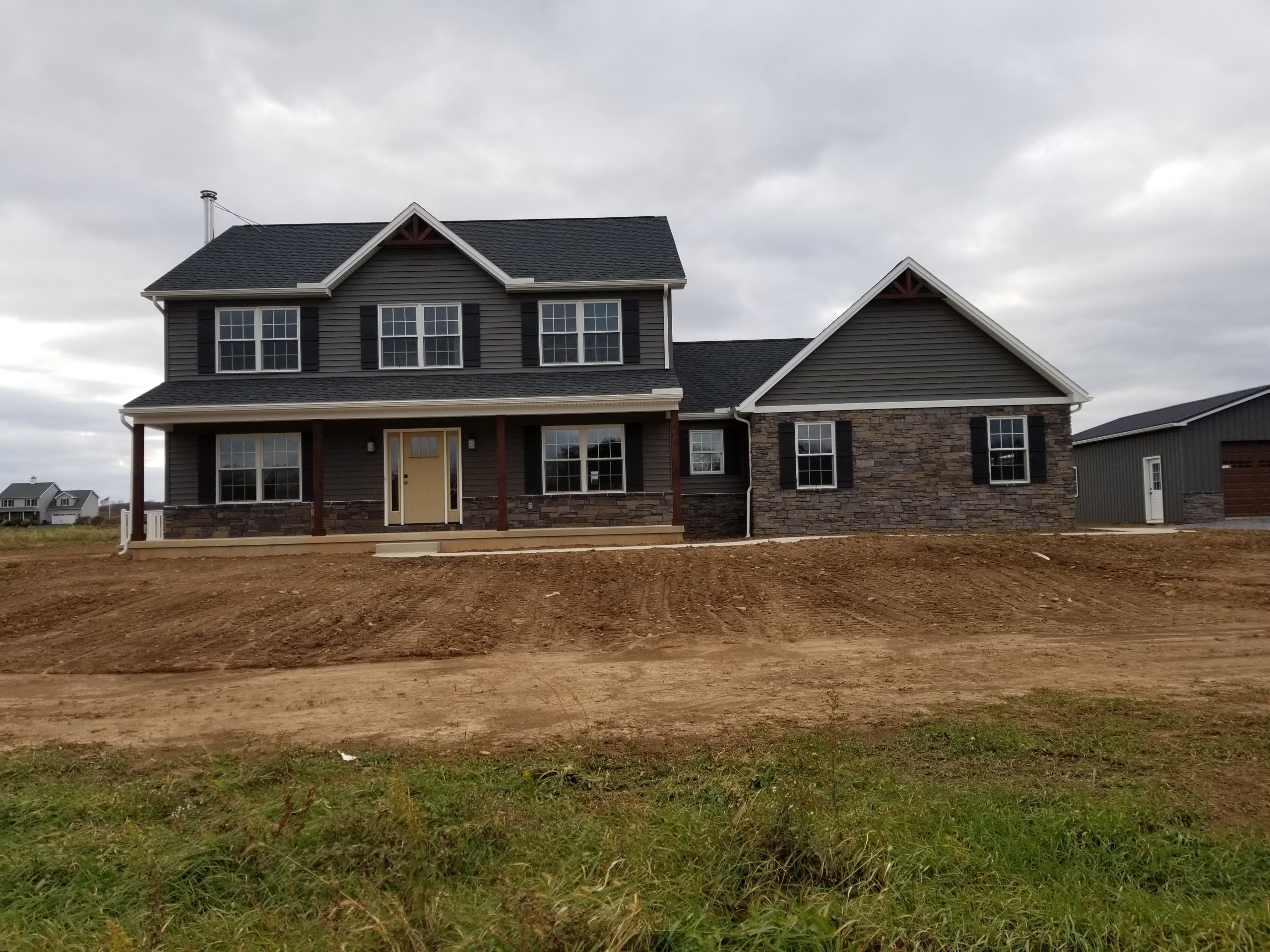 Front exterior view of a new home with dark gray siding, black shutters, stone siding, white trim, an attached garage, and black roofing.