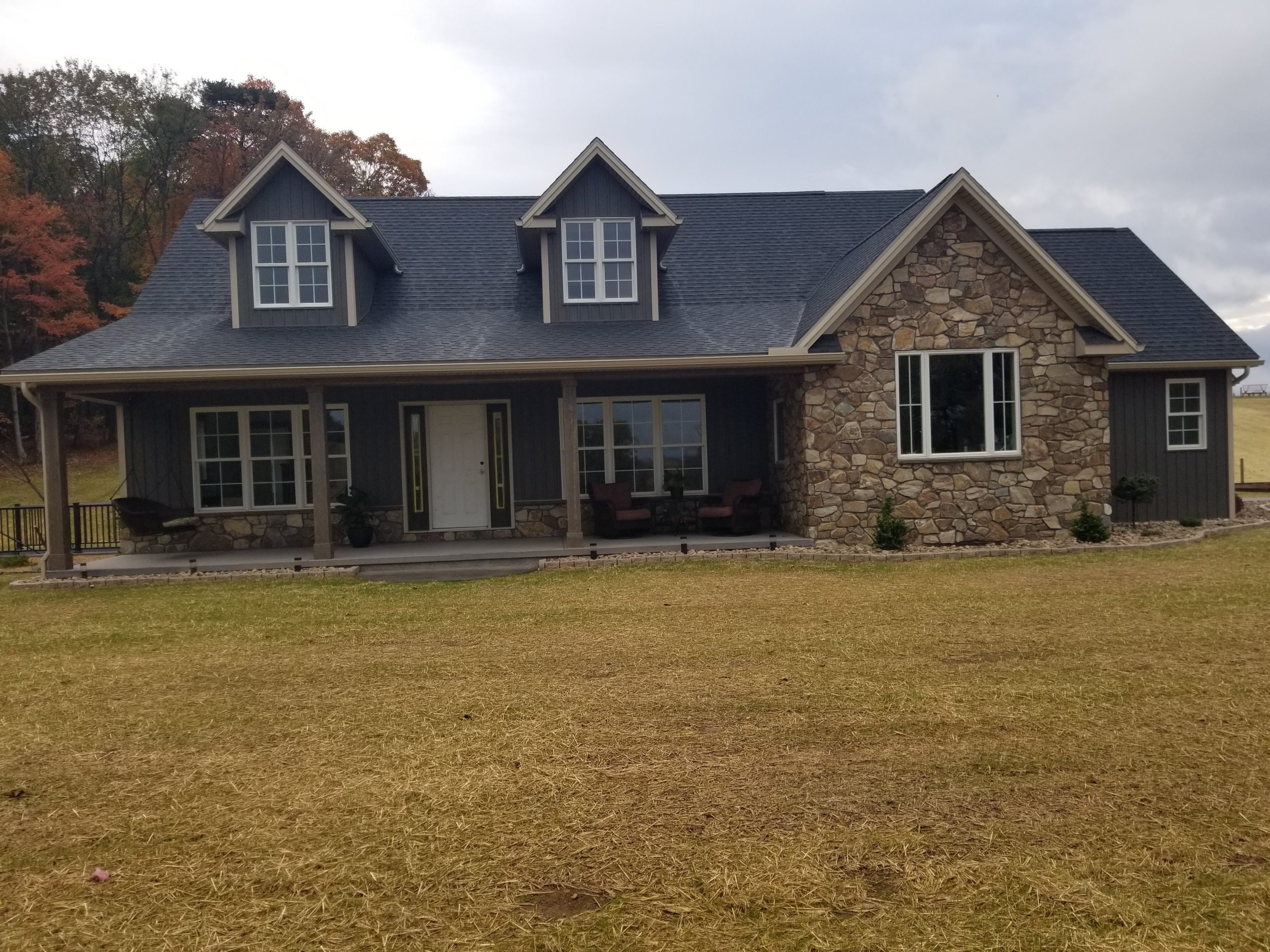 Front exterior view of a new home with dark gray siding, black roofing, stone accents, and a covered front porch.
