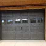 Close up of a black garage door with six sets of double windows on a garage with rustic wood siding.