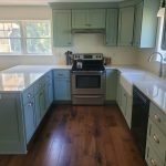 Renovated kitchen with green cabinets, a white counter top, stainless steel oven, a black dishwasher, and a white farmhouse sink.