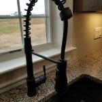 Close up of a black flexible kitchen sink faucet in front of a window overlooking the home's yard.