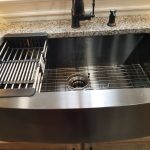 Close up of a stainless steel kitchen sink with speckled granite countertops, a black kitchen faucet, and a utensil drainer holder in the sink.
