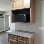 Microwave corner in a kitchen with a black microwave and stained brown cabinets with a speckled granite countertop.