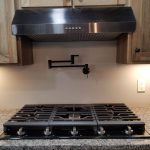 Close up of a stove range top and a black adjustable water faucet for filling pots that is attached to the kitchen wall above the stove.