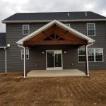 Close up of an a-frame covered back porch on a new home with dark gray siding and white trim.