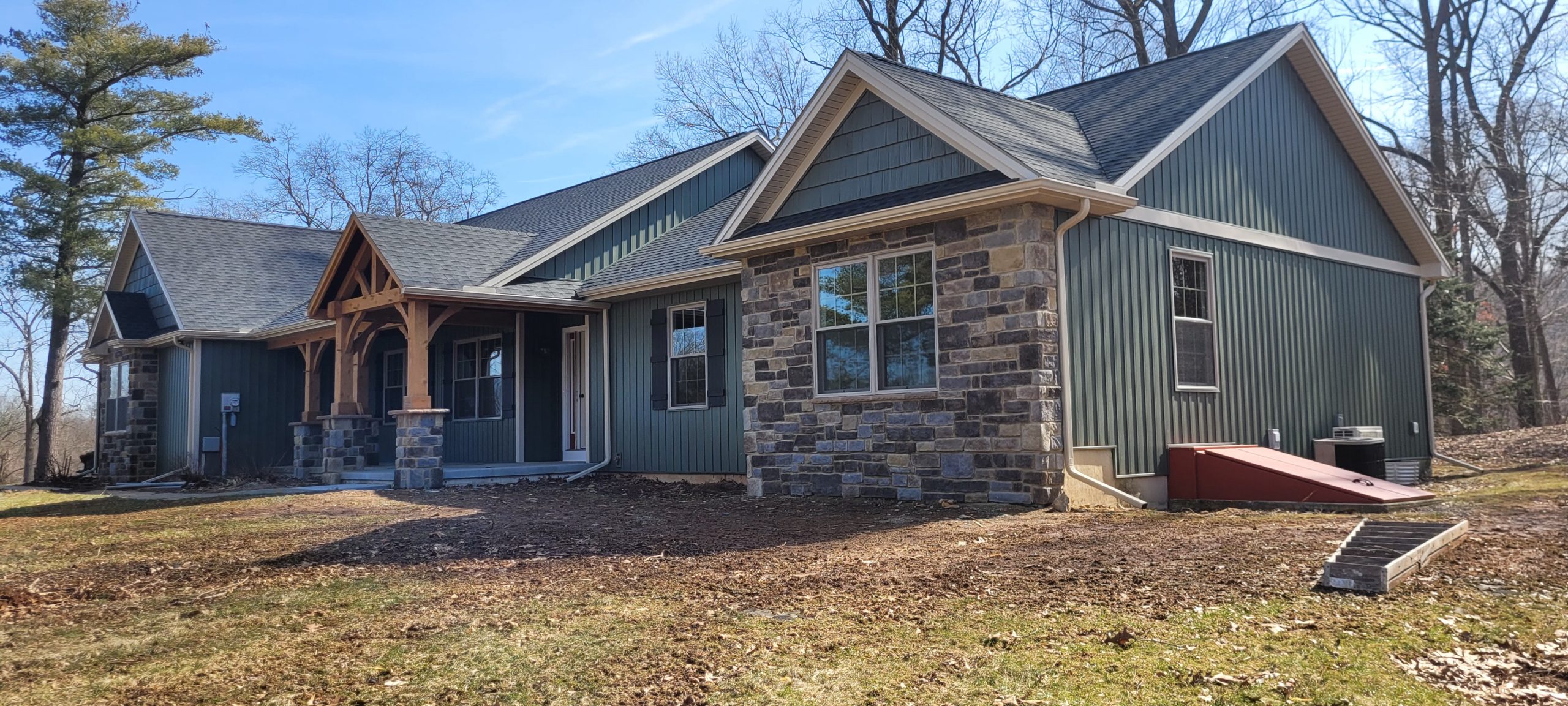 Photo of home front exterior after remodel with green vinyl siding, stone siding accents, white trim, and black shutters.