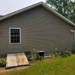 Side view of a home before its remodel with tan siding, a rusted basement entrance, white trim, and a window.