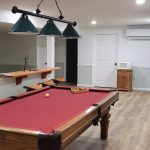 Finished basement with a pool table, 3-light pendant light, and wood flooring.