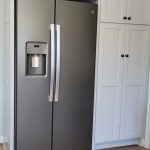 Built in white wood pantry cabinets around a silver double door fridge.
