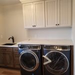 Blue washer and dryer in a laundry room with wood cabinets, wood flooring, white countertops, and a sink.