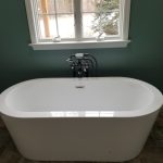 Close up of a white soaking tub in front of a white window and dark green walls.