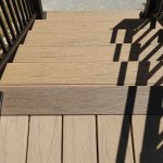 Close up of new, tan deck stairs with black railings.