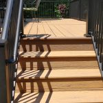 Close up of new, tan deck stairs with black railings.