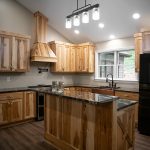 A kitchen with natural wood cabinets, a natural wood kitchen island, hardwood flooring, tan walls, and a large black fridge.