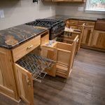 Close up of natural wood kitchen cabinets with dark quartz countertops, and built-in cabinet organizers.