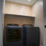 Close up of a black washer and dryer in a small laundry room with a shiplap accent wall.