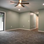 Room with sage green walls, white trim, a white ceiling, a brown ceiling fan with a light, gray carpeting, and a glass sliding door leading outside.