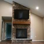 Living room with tan walls, hardwood floors, and a large stone fireplace with a mounted tv and floating wood beam shelf.