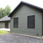 Back exterior of a home with green siding, black trim, black windows, black doors, and black asphalt roofing.