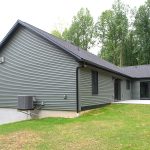 Back exterior of a home with green siding, black trim, black windows, black doors, and black asphalt roofing.