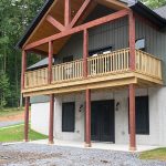 Front exterior view of a 2-story home with a white first story, green second story, black windows, black doors, and a second story covered wood deck.