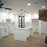 Kitchen with light gray walls, white trim, vinyl plank flooring, white cabinets, a white kitchen island with a black sink faucet, and black sliding doors with glass.