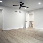 Bedroom with light gray walls, white trim, vinyl plank flooring, 3 open doors, and a black ceiling fan.