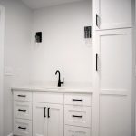 Bathroom with light gray walls, vinyl plank flooring, a white sink vanity, a black sink faucet, and a set of white stacked cabinets connected to the sink vanity.