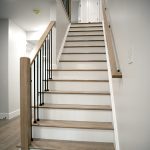 White and light brown wood staircase with matching wood railings and black balusters.