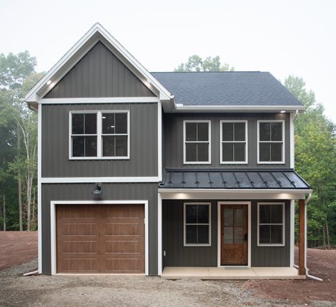 Front exterior view of a 2-story home with dark gray siding, white trim, a brown garage door, a covered front porch, and a brown front door.