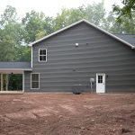 Left side exterior view of a 2-story home with dark gray siding, white trim, a white single-entry side door, and a covered back patio.