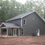 Back and left side exterior view of a 2-story home with dark gray siding, white trim, a white single-entry side door, and a covered back patio.