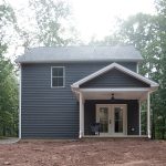 Back exterior view of a 2-story home with dark gray siding, white trim, and a covered back patio with white double doors.