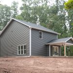 Back and right side exterior view of a 2-story home with dark gray siding, white trim, and a covered back patio with white double doors.