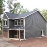 Front and right side exterior view of a 2-story home with dark gray siding, white trim, a brown garage door, a covered front porch, and a brown front door.