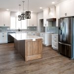 Kitchen with light colored walls, vinyl plank flooring, light blue chevron tile backsplash, white cabinets, stainless steel appliances, and a wood base kitchen island.