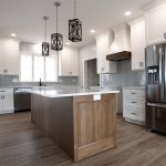 Kitchen with light colored walls, vinyl plank flooring, light blue chevron tile backsplash, white cabinets, stainless steel appliances, and a wood base kitchen island.