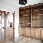 Side room with glass panel wood double doors, light colored walls, vinyl plank flooring, and a large built-in wood bookshelf with 3 sets of cabinets.