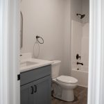 Bathroom with light colored walls, vinyl plank flooring, a dark blue sink vanity with white stone countertop, a white toilet, and a white shower-tub combo.